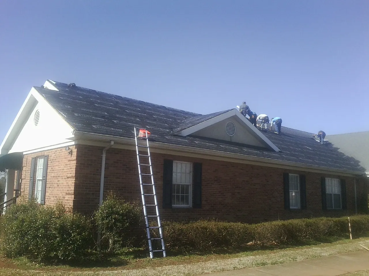 Crew tearing shingles off a brick ranch roof with a ladder set — Metal Roof Repair work by our crew in Maple Hill