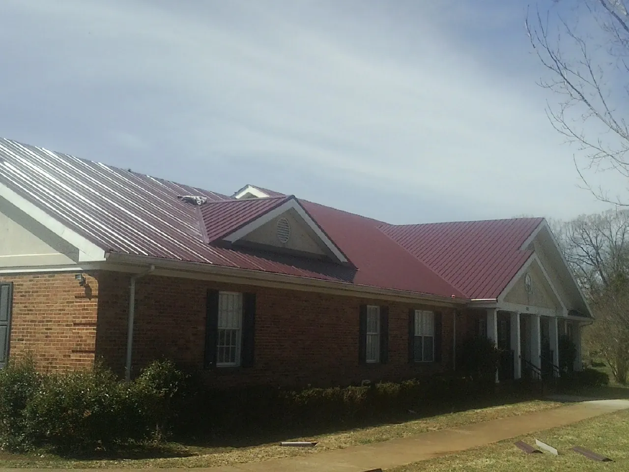 Red metal roof with gabled entries on a long brick building, from a Hail Damage Roof Repair job in Maple Hill