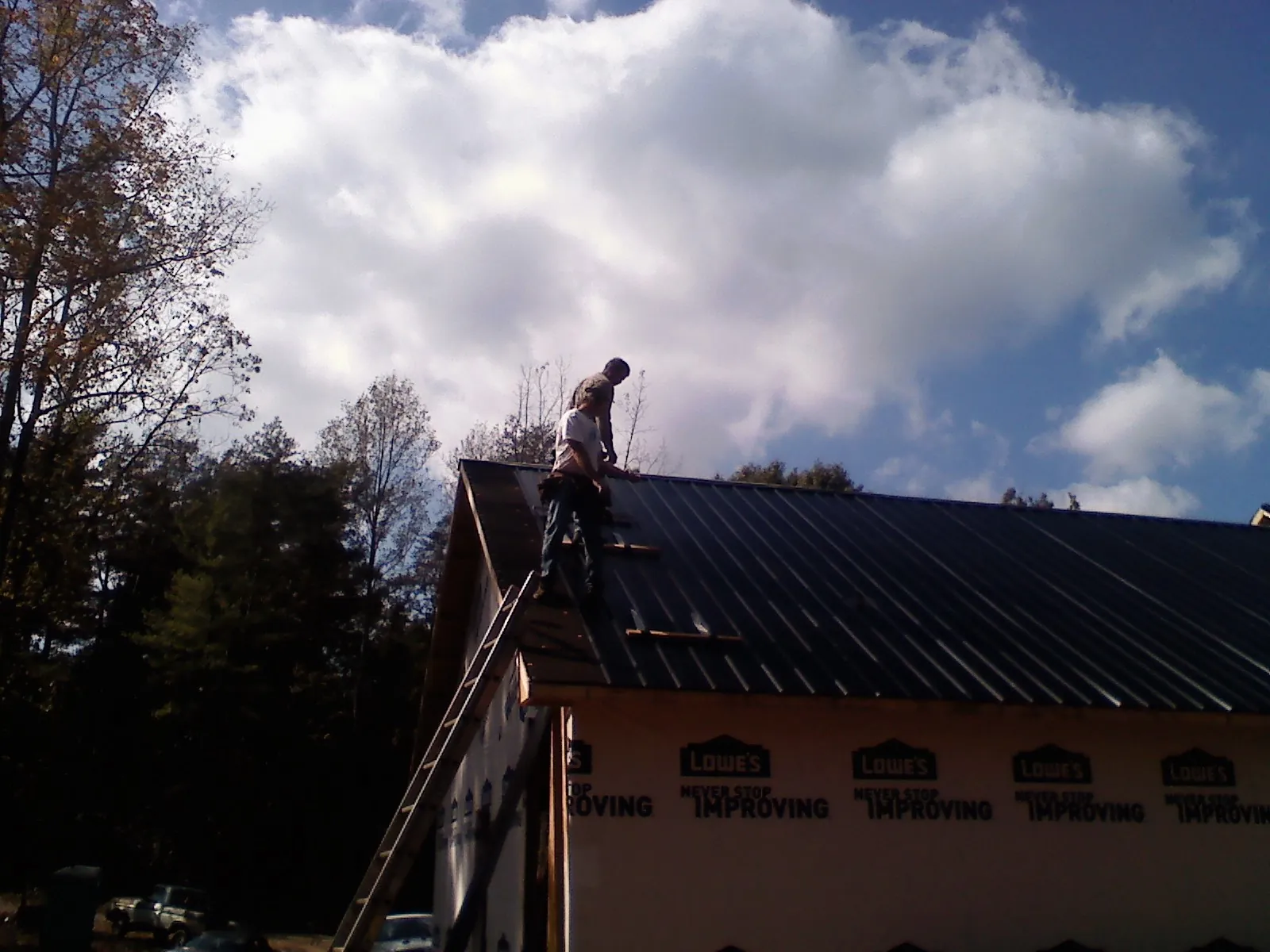 Roofer fastening dark metal panels high against a cloudy sky, from a Roof Inspection job in Maple Hill
