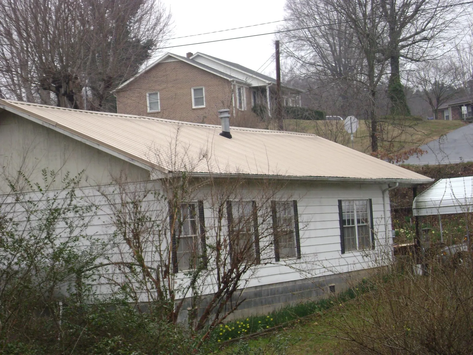 Tan metal roof on a white sided house set into a hillside — Commercial Roofing by Roofing Brothers in Maple Hill