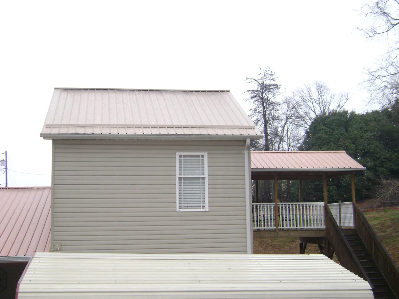 Tan metal roofs on a two story addition and attached porch, from a Roof Replacement job in Maple Hill